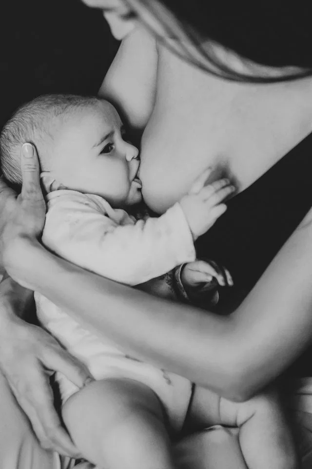 Primer plano de las manos de una madre sosteniendo la cabeza de su bebé mientras se prende al pecho