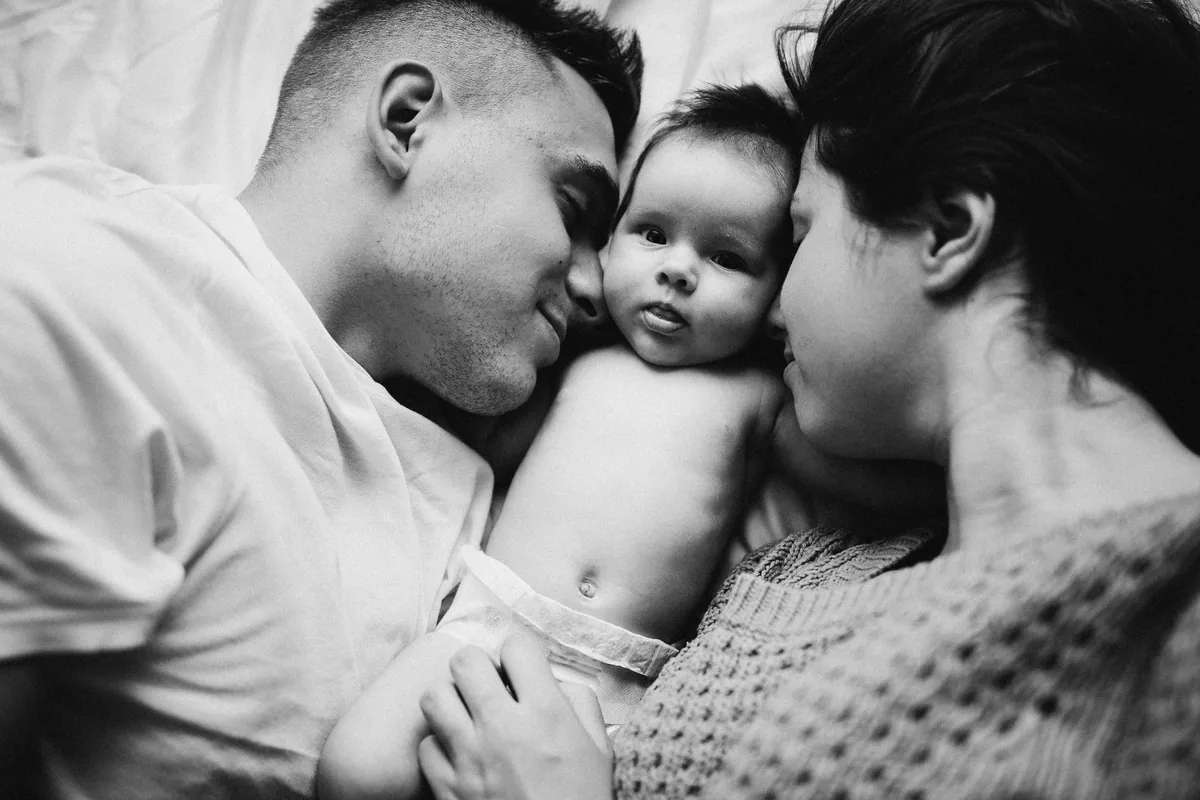 Pareja sentada junta en el sofá con el bebé dormido entre ambos, momento tranquilo